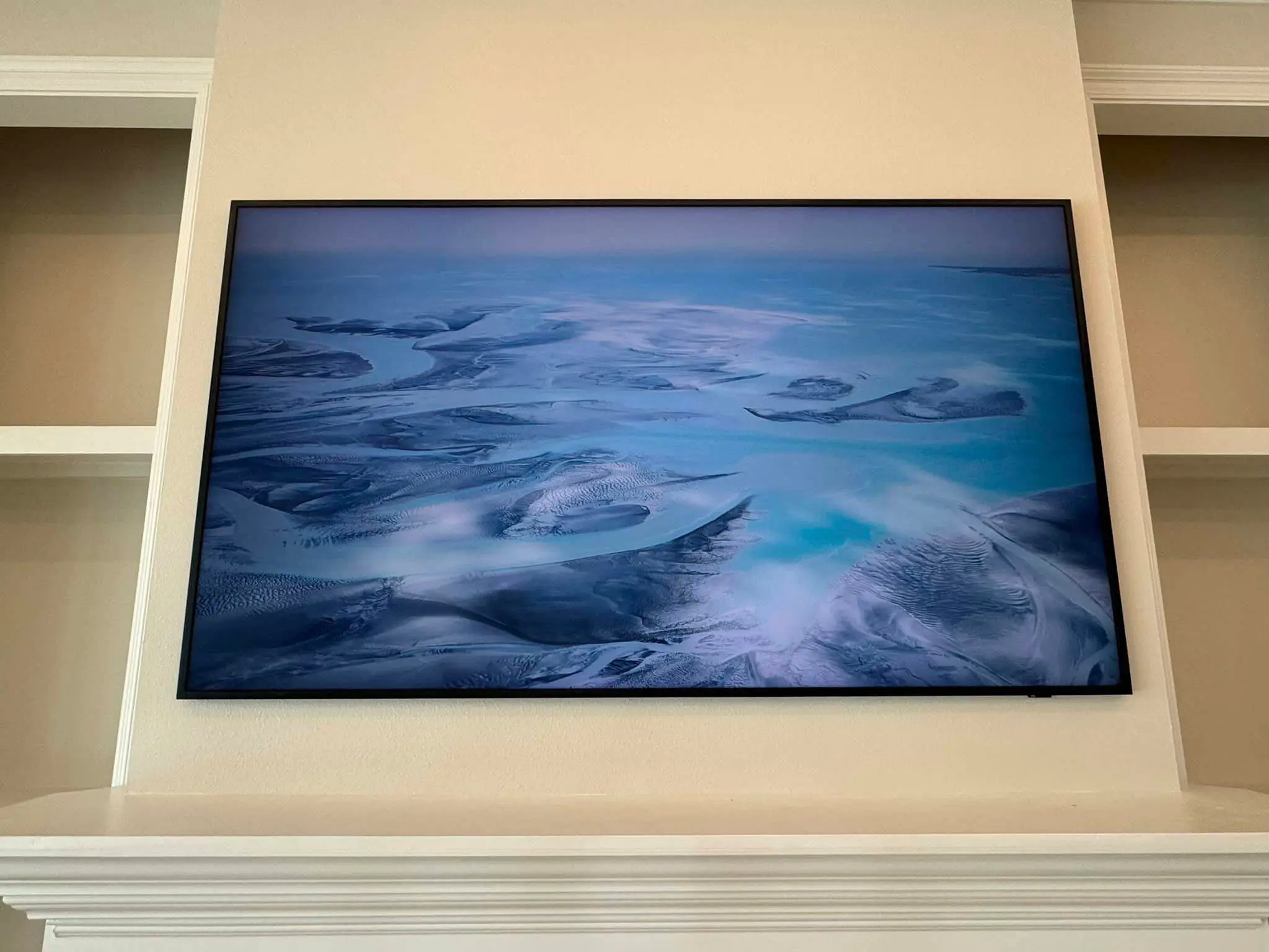 Wall-mounted television centered on a gray shiplap wall between framed photos.